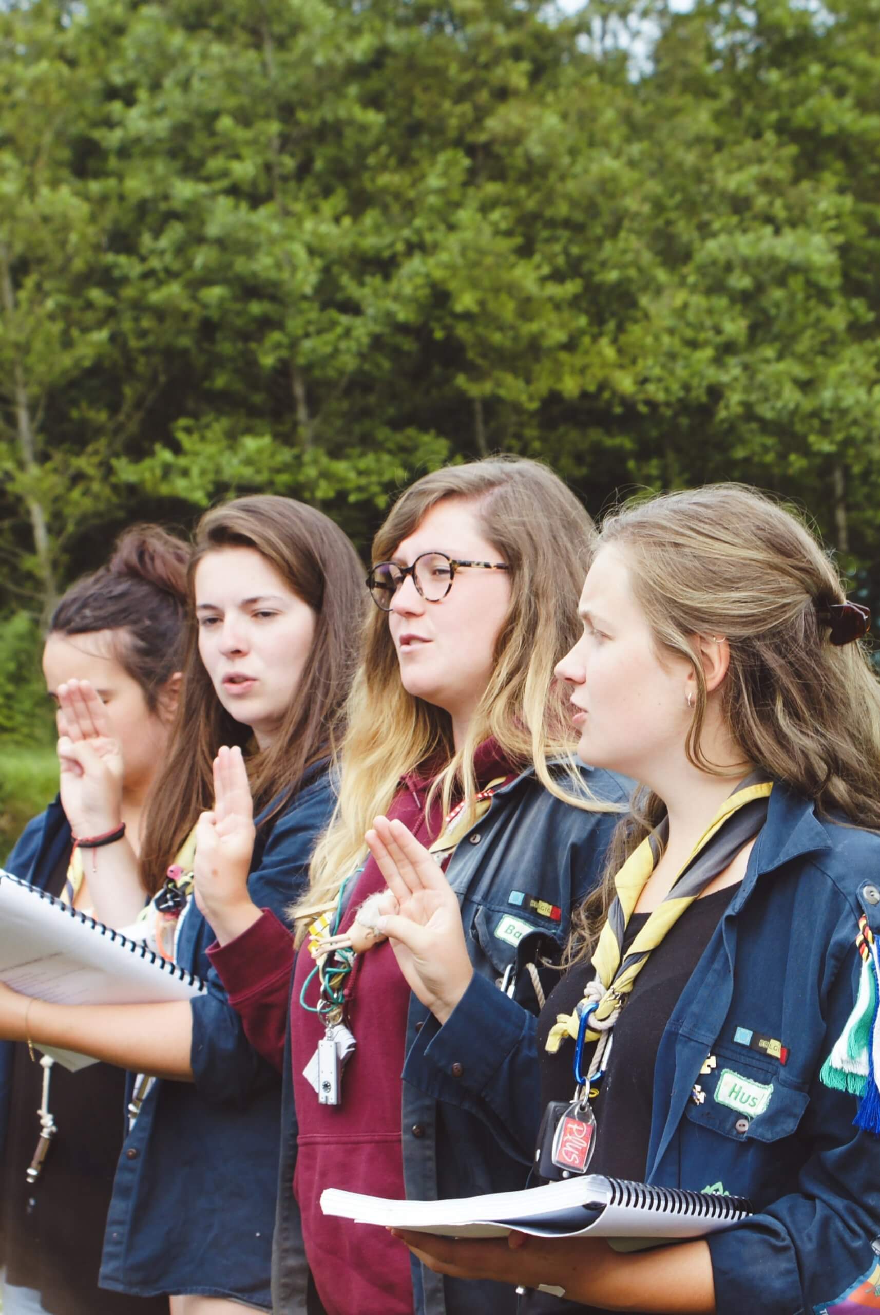 A group of four Girl Scouts saying their pledge with the Girl Scout hand sign