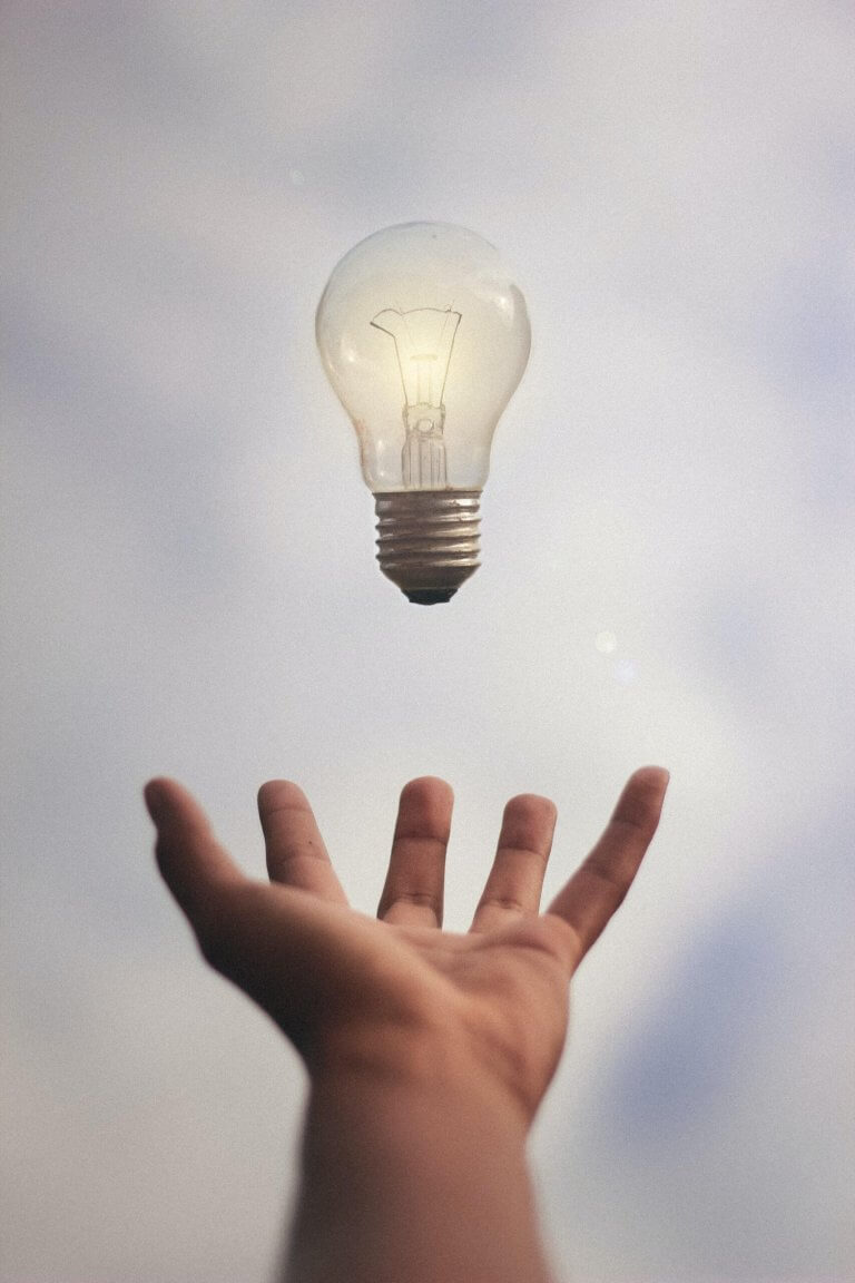 A bright lightbulb floats over an outstretched hand