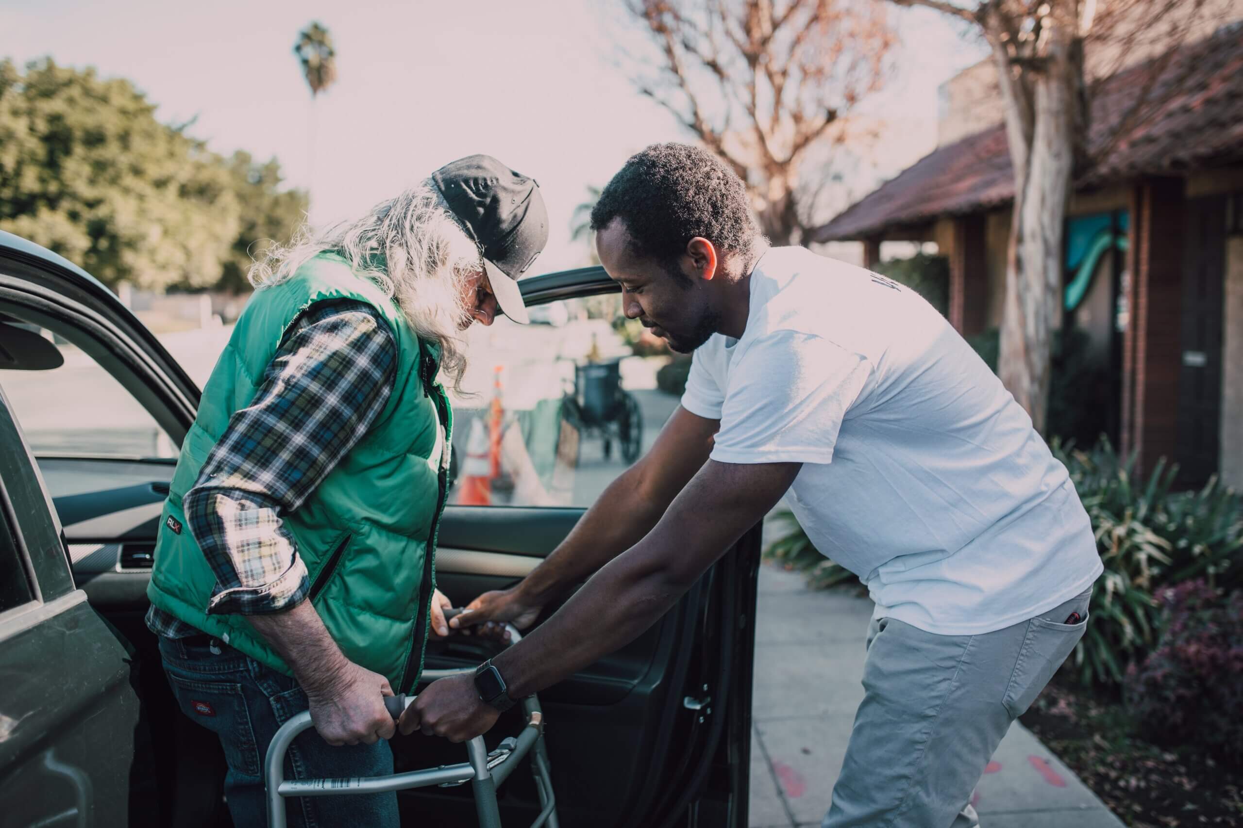 Volunteer helping elderly man out of car.
